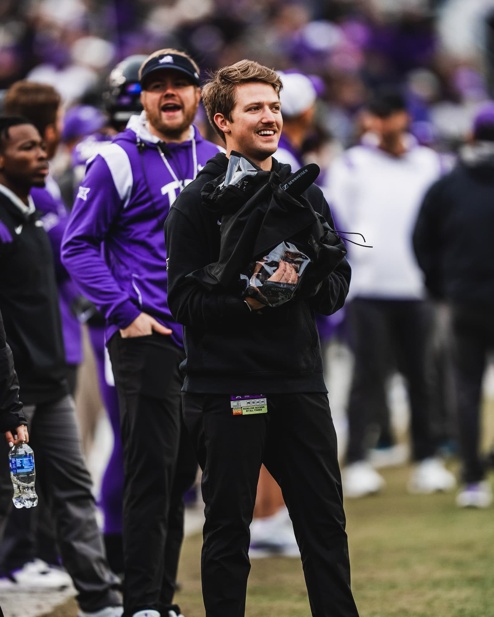 Luke Heslep smiling on a football sideline with a rain-covered camera and shotgun microphone