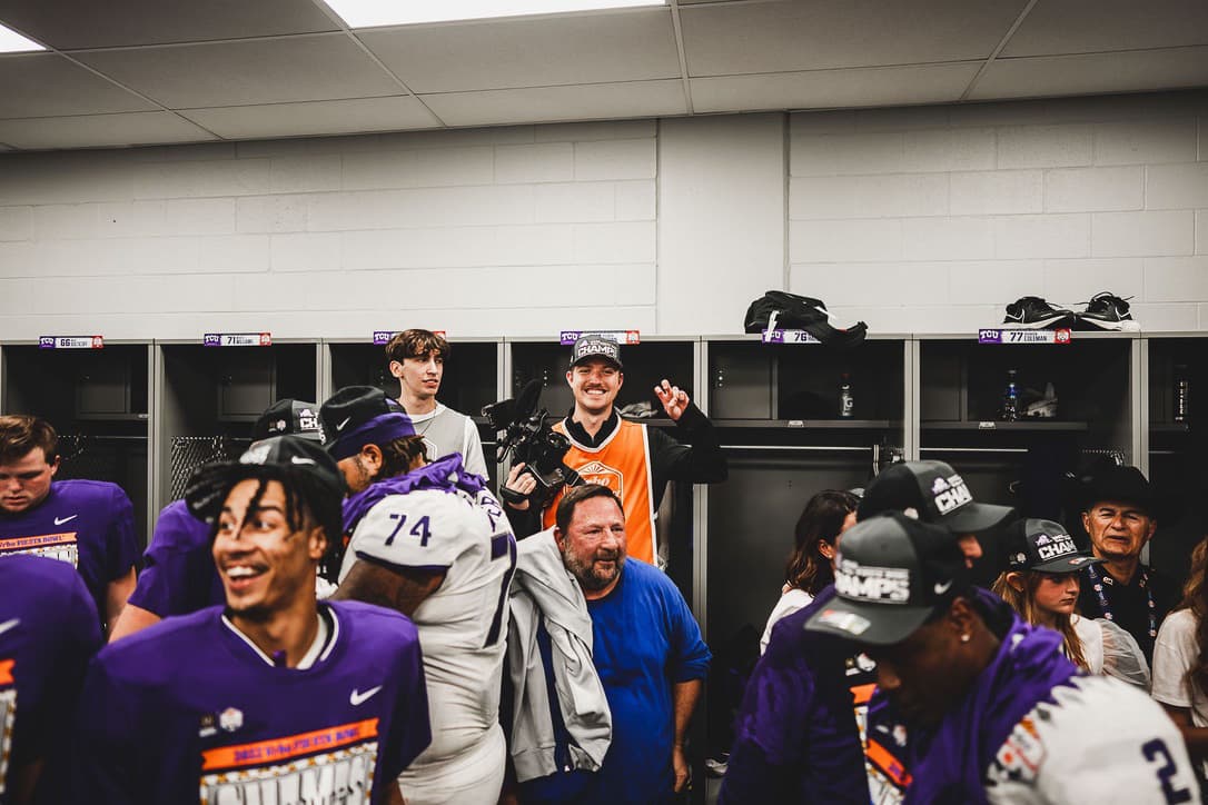 Luke Heslep in an orange media vest celebrating with TCU players in a Fiesta Bowl championship locker room