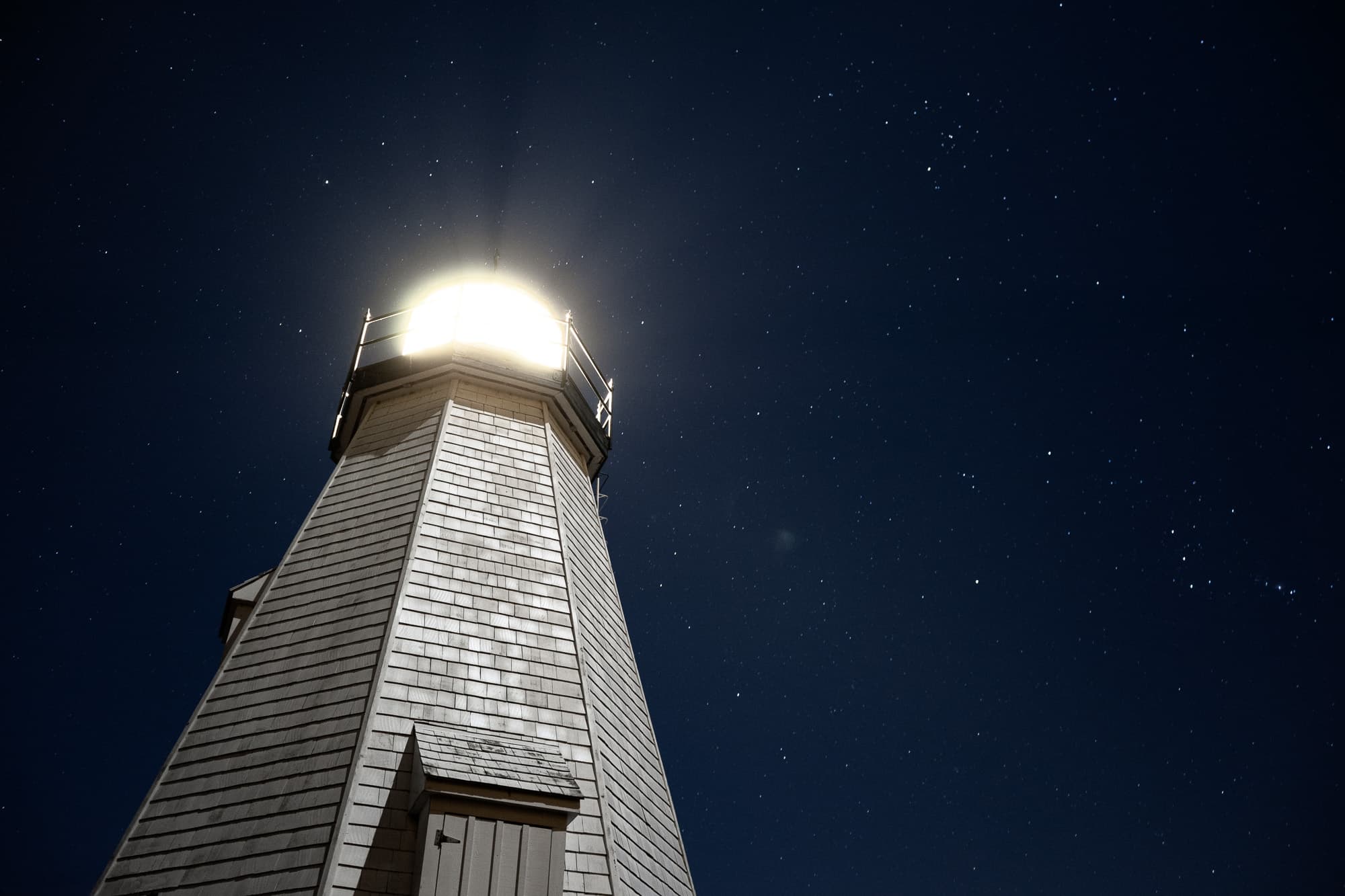 A lighthouse tower and its beacon against a field of stars
