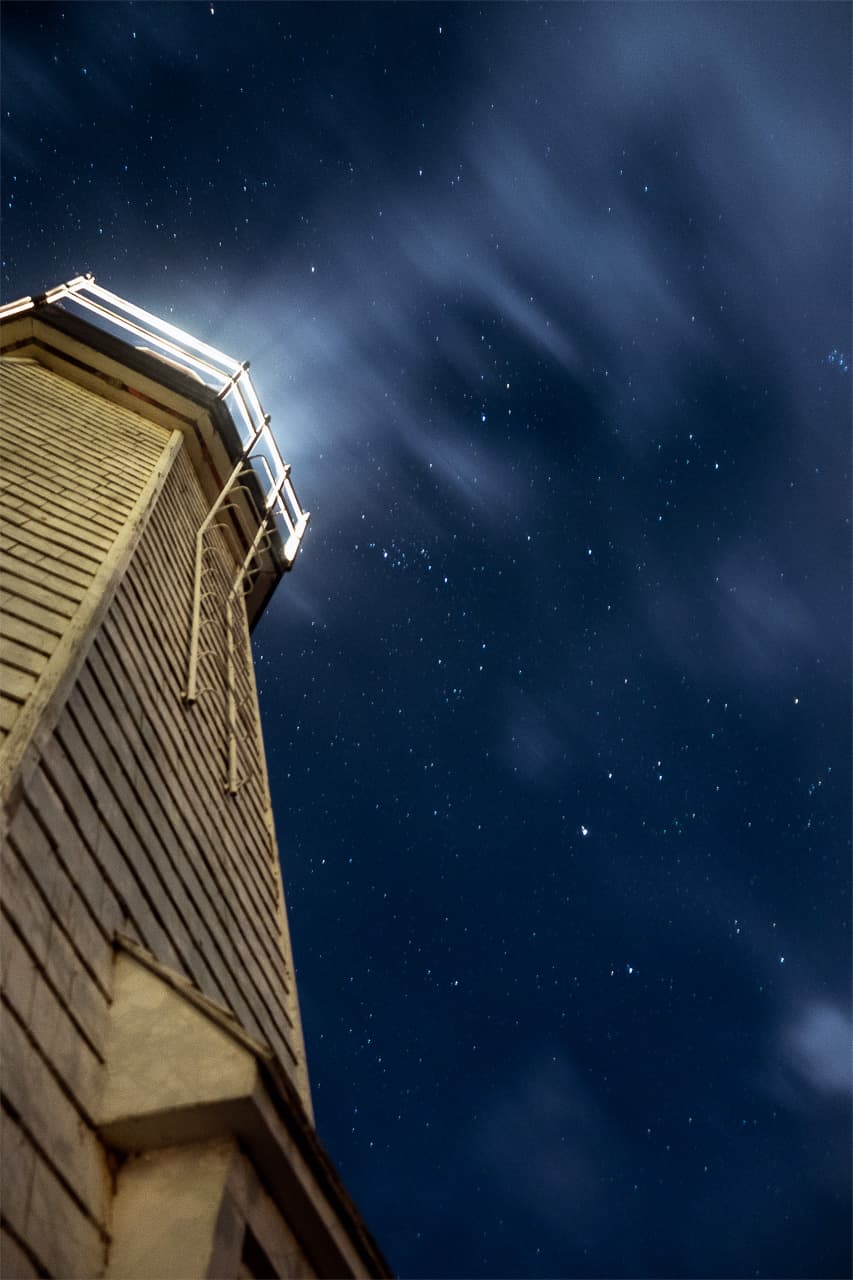 The lantern gallery of a lighthouse against a star-streaked sky