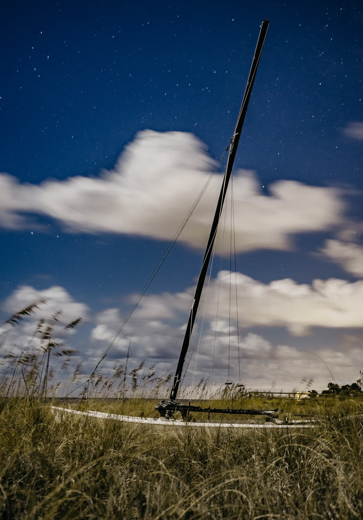 A beached sailboat in dune grass under moonlit clouds