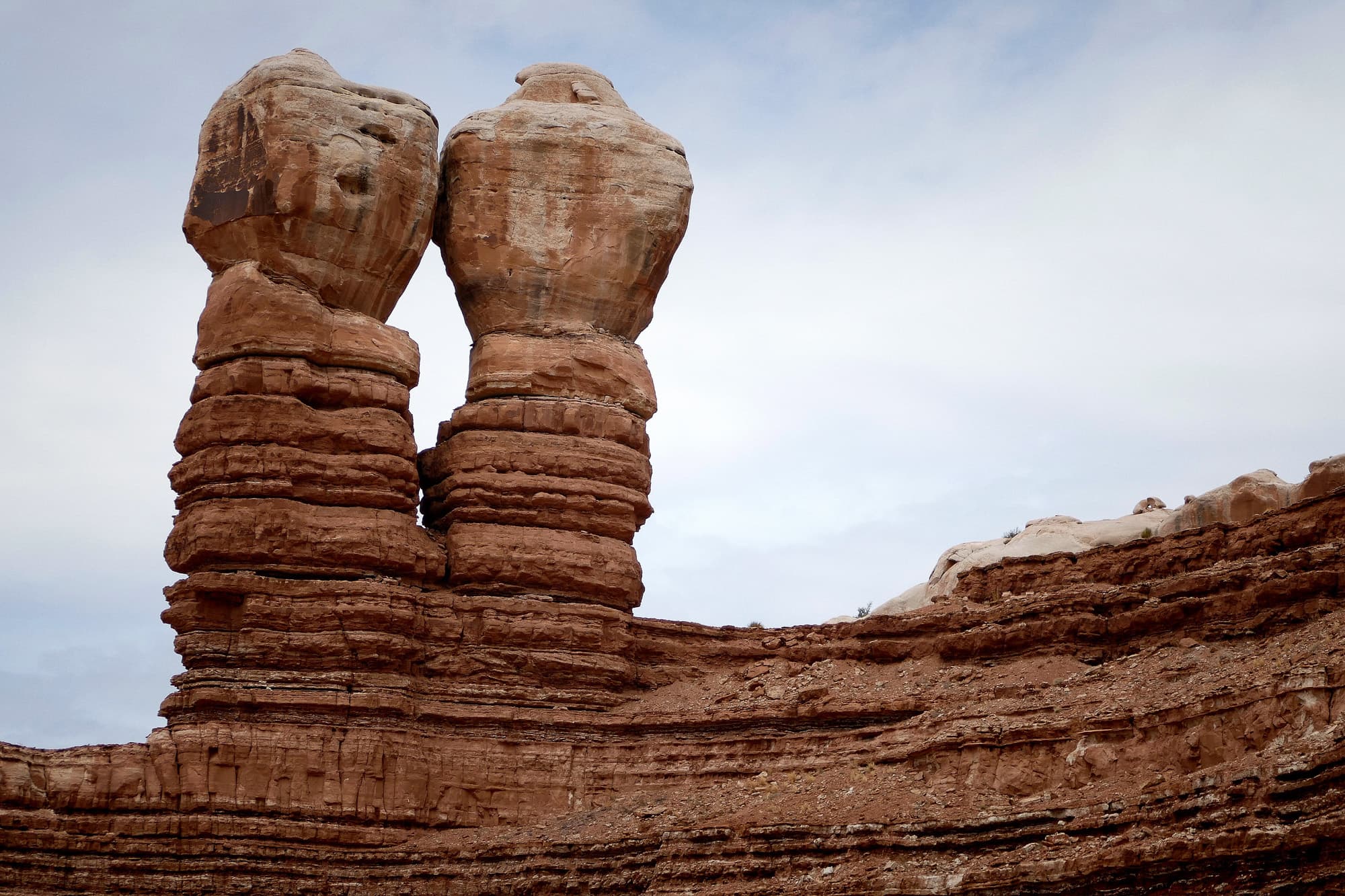 Two sandstone pillars with weathered caprocks on a layered shelf
