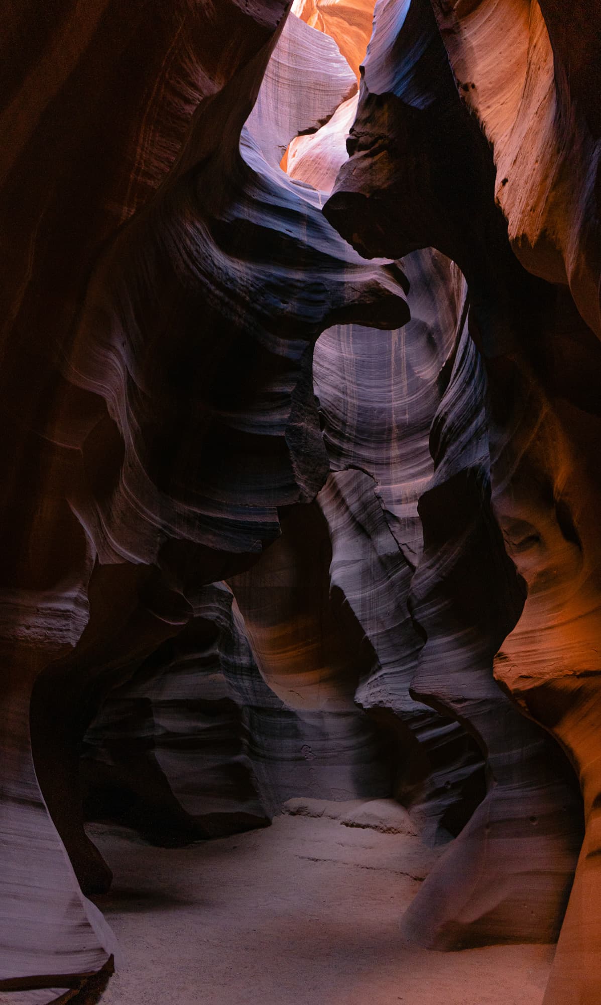 Slot canyon walls rising from a sandy floor toward the light