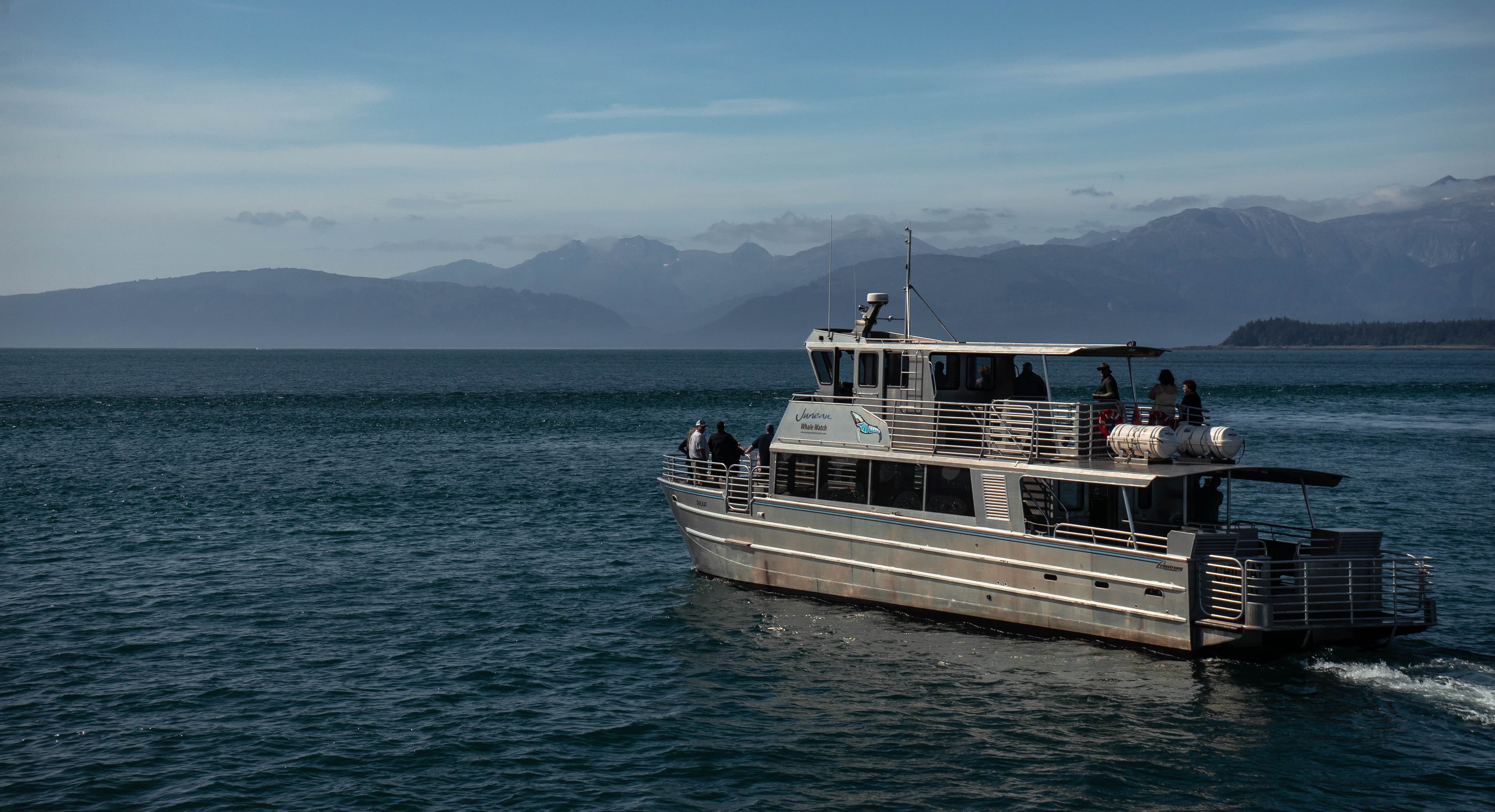 Whale-watch boat on open water with mountain backdrop