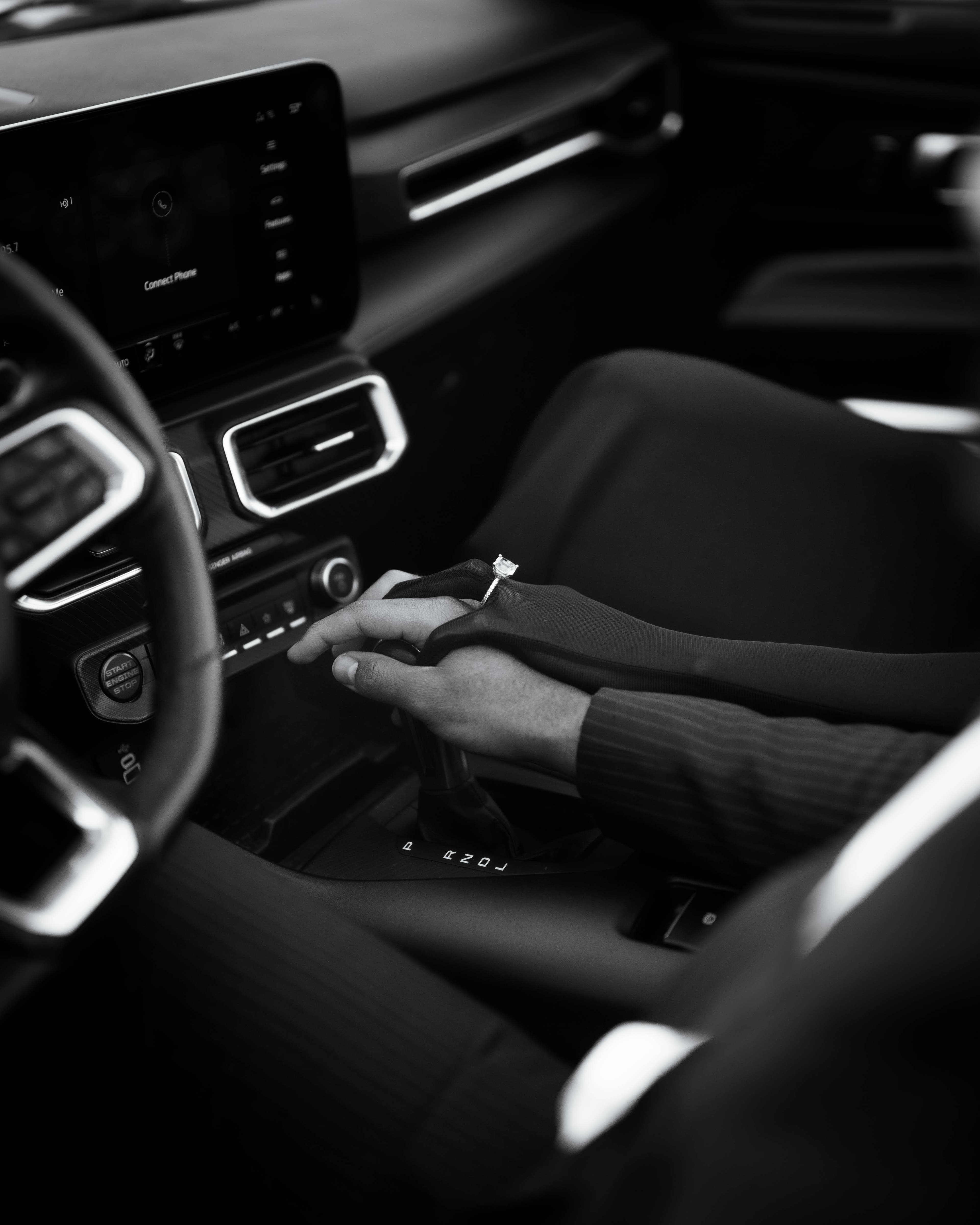Black and white detail of hands and an engagement ring inside a car