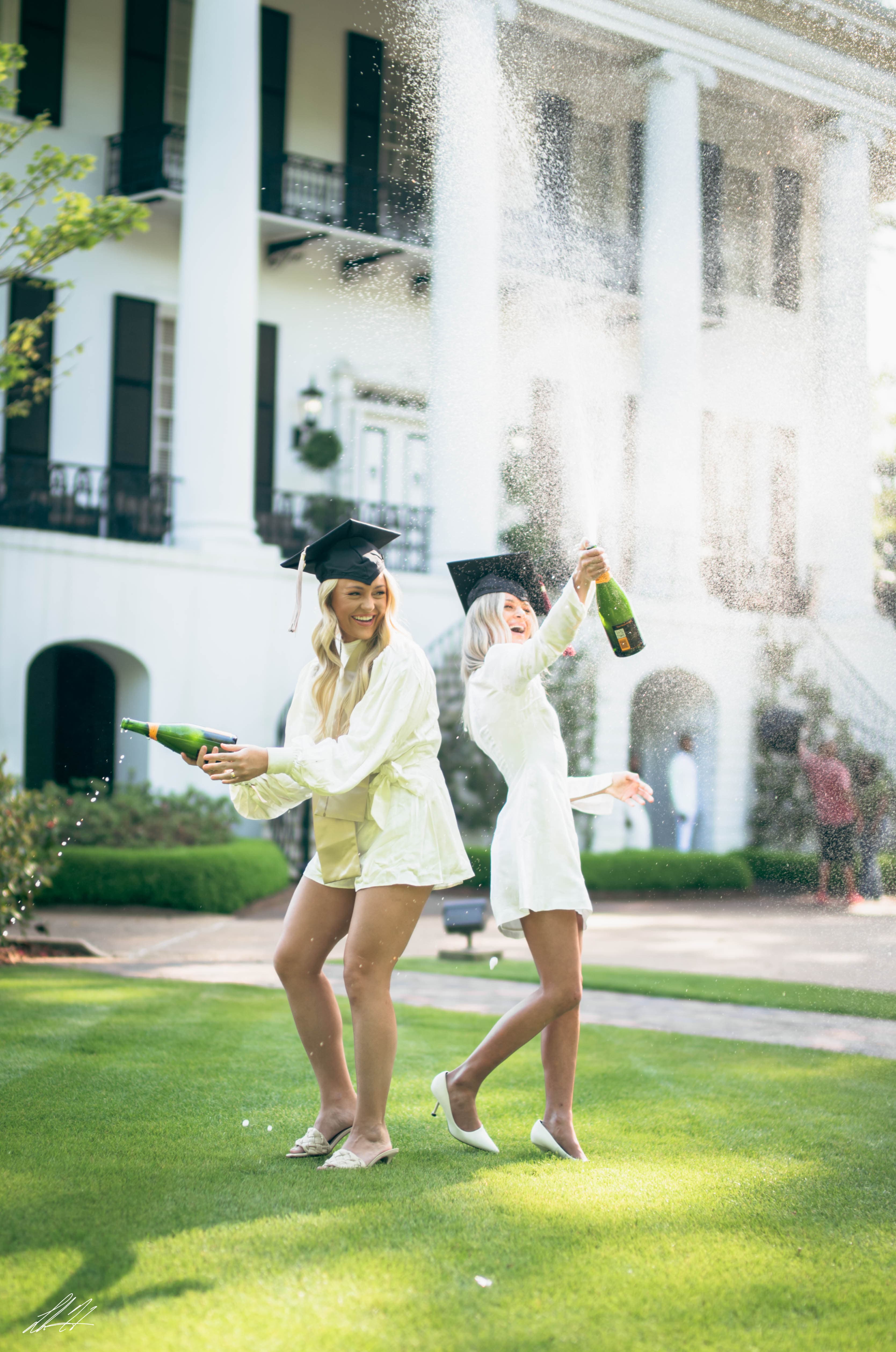 Two graduates celebrating with champagne spray on a green lawn