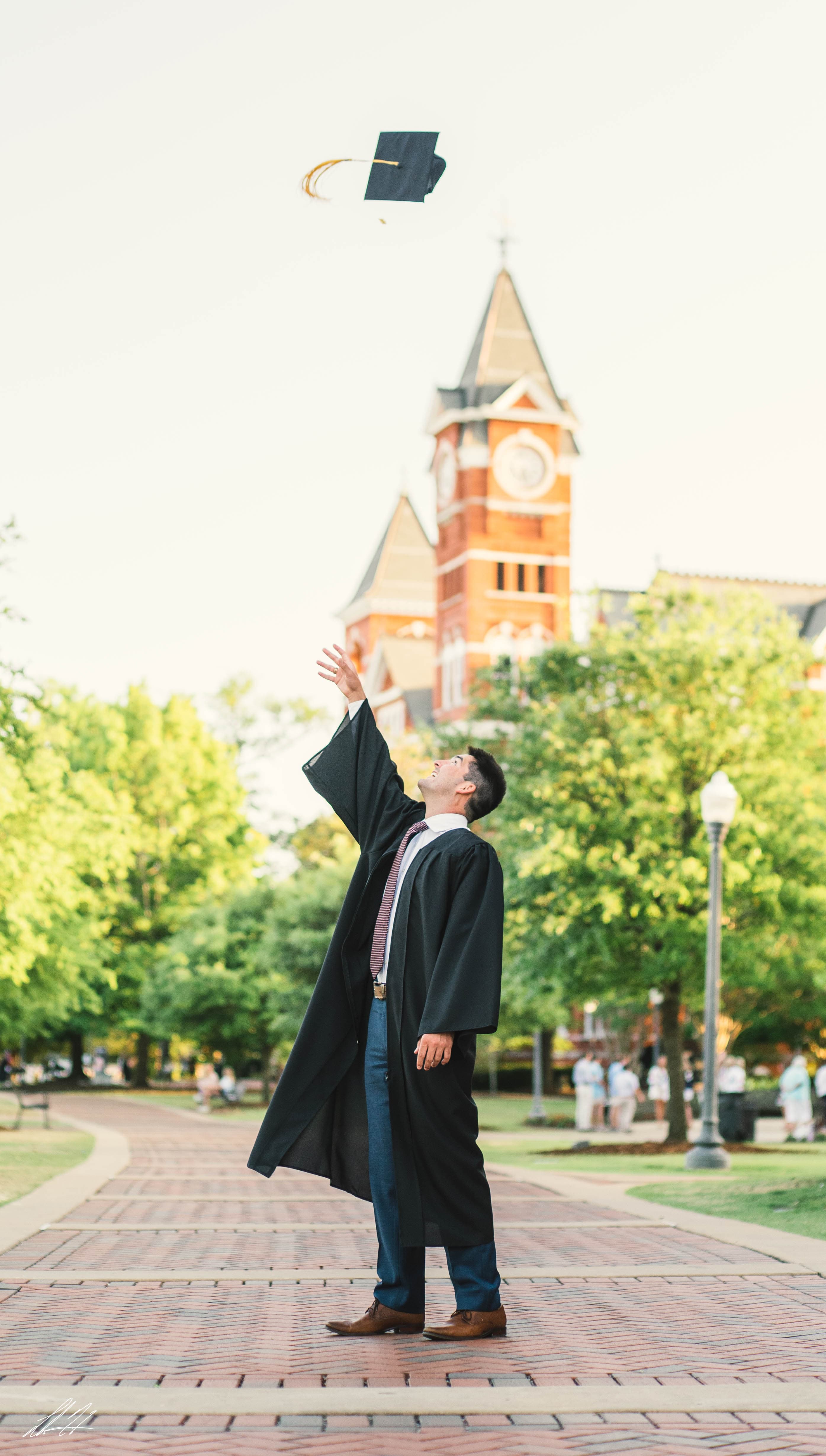 Graduate tossing a cap in front of a brick clock tower