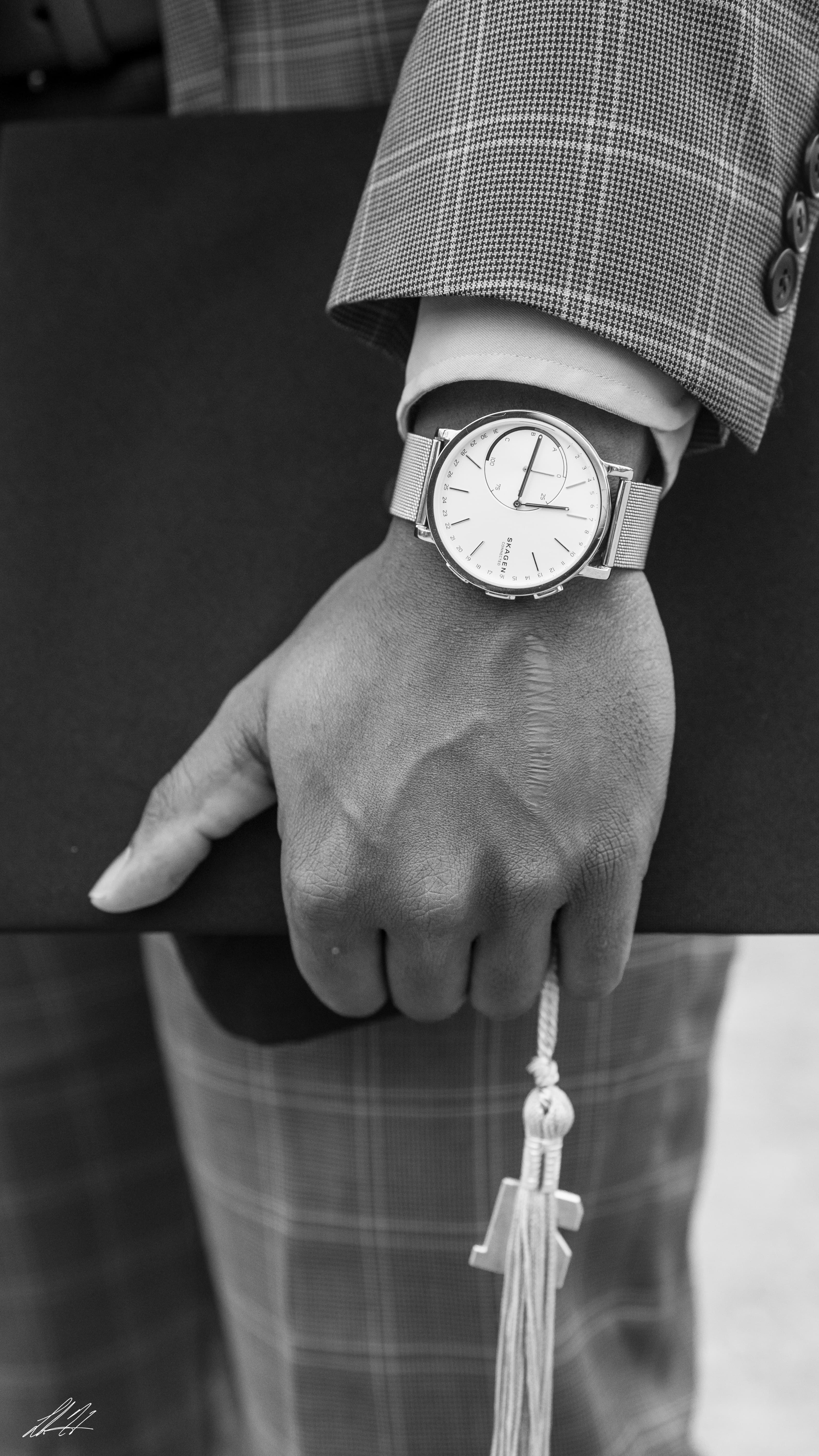Black and white detail of a watch, hand, and graduation tassel