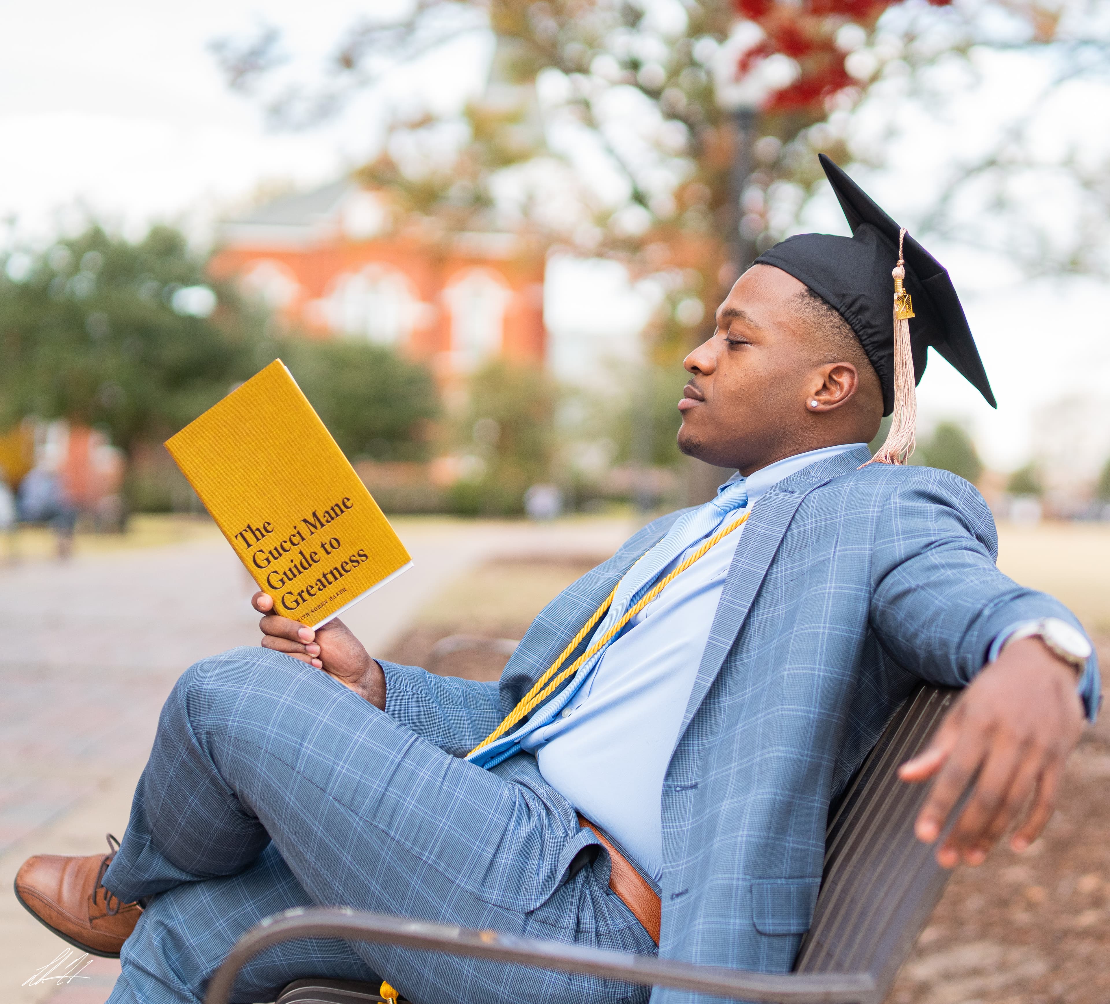 Graduate in a light blue suit reading on a campus bench
