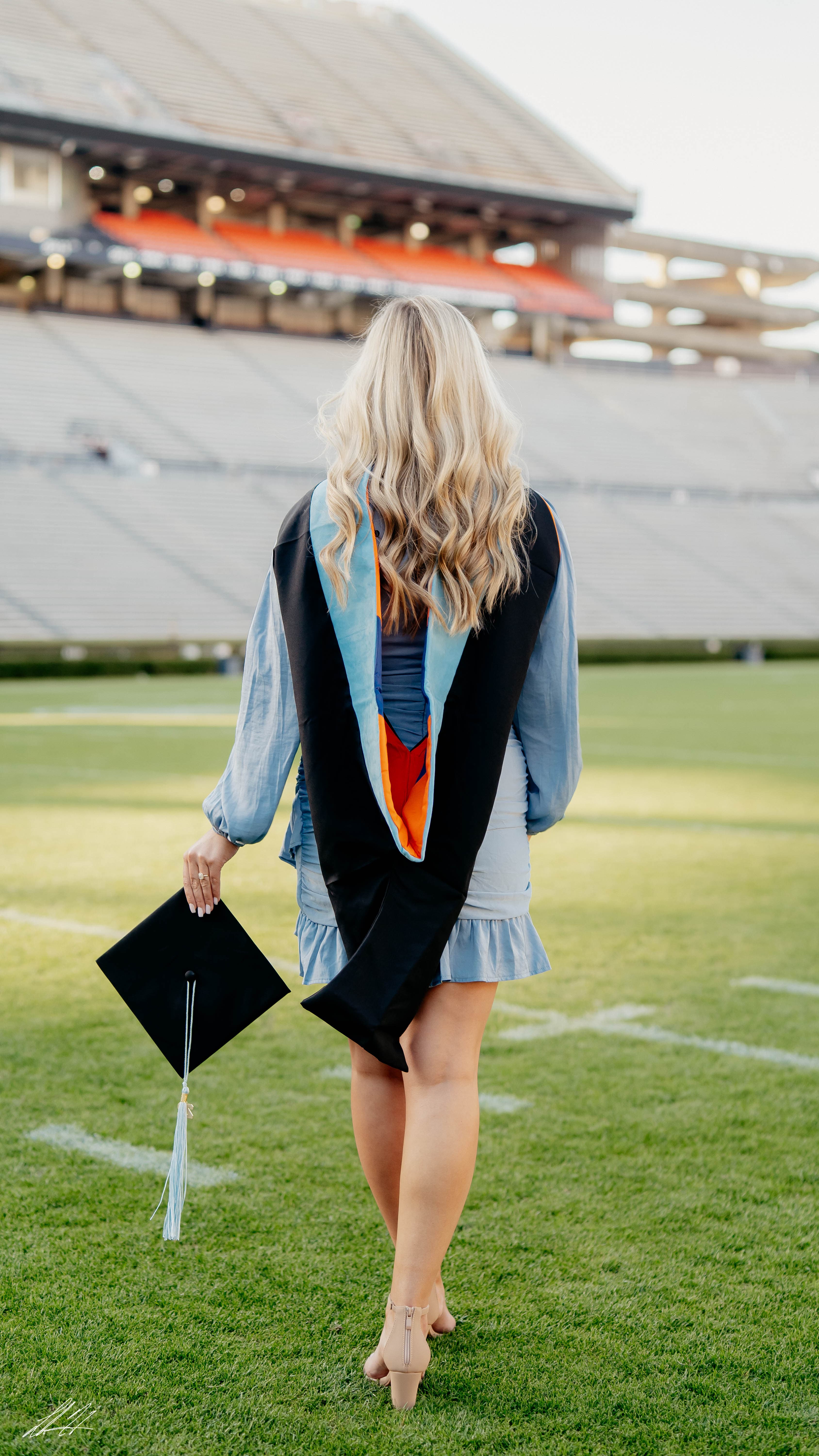 Graduate walking across a stadium field carrying a mortarboard