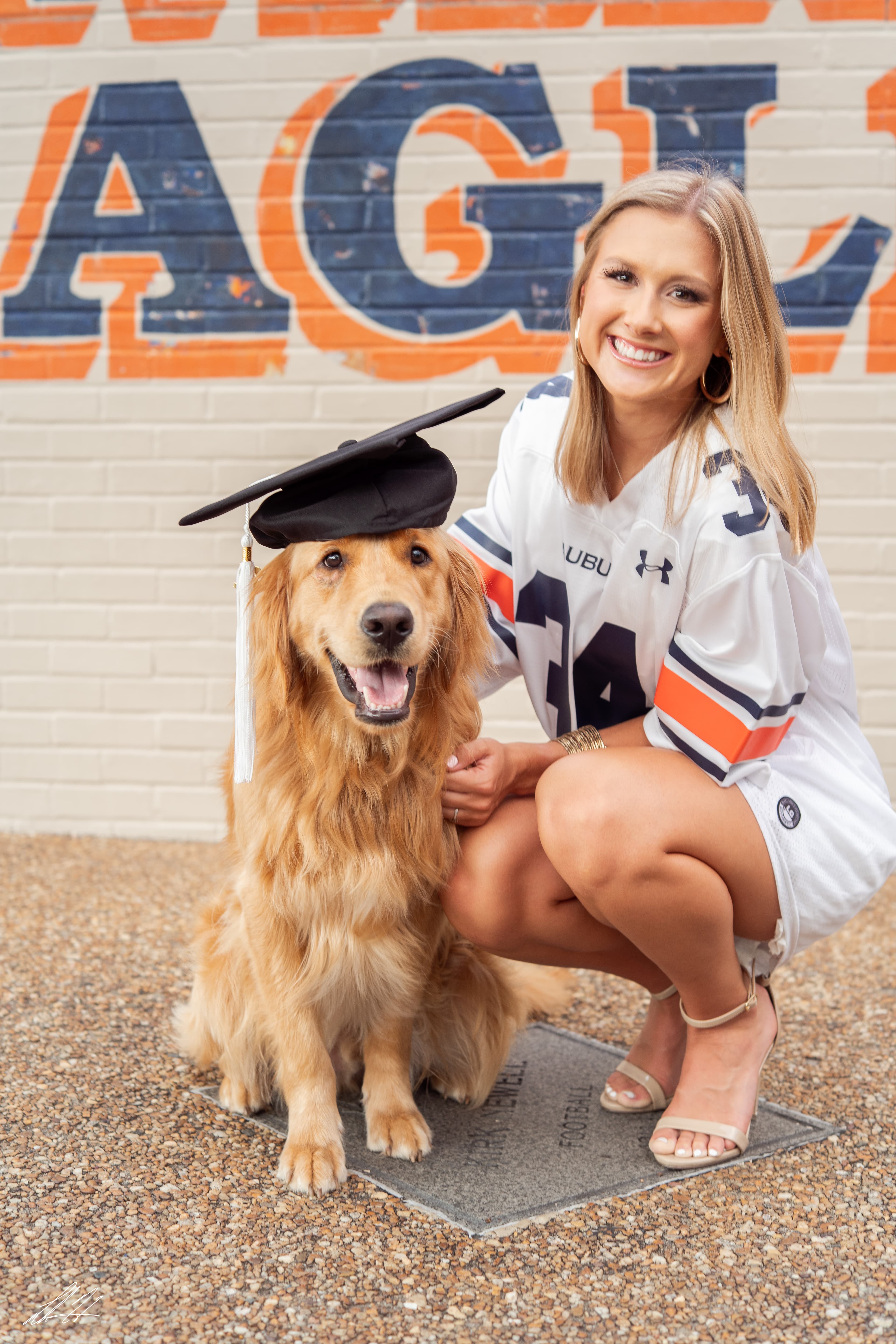 Graduate kneeling beside a Golden Retriever wearing a mortarboard