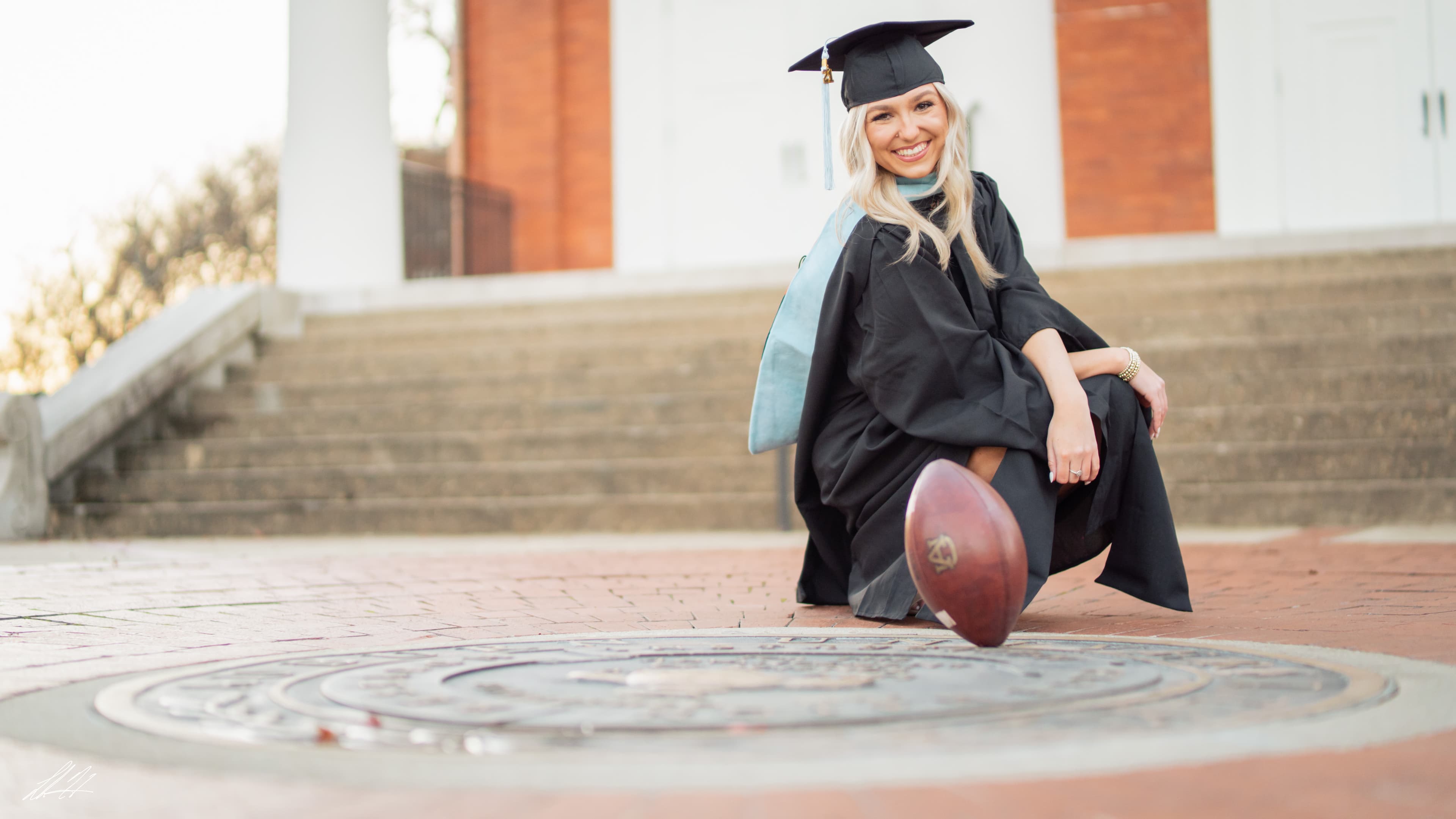 Graduate kneeling by a university seal with a football in the foreground
